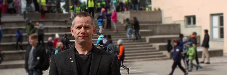 Per Hansson på en skolgård med elever i bakgrunden